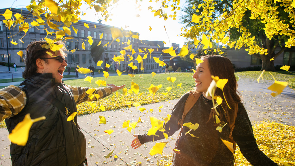 Two Students Playing in the Leaves on Campus in the Fall. 